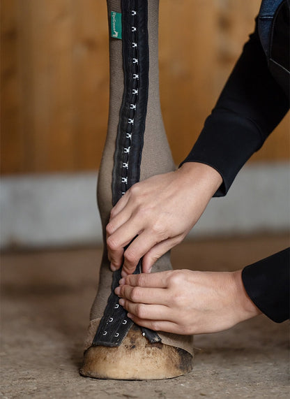 Detailansicht der EquiCrown med Silver Maßbandage. Die Bandage wird gerade am Pferdebein mit ihrem Hakenverschluss geschlossen.